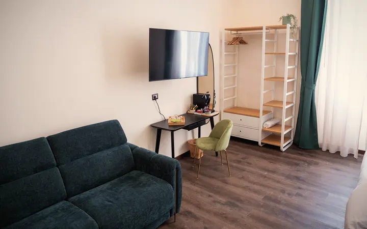 Il divano di velluto, lo scrittoio e la TV di una camera quadrupla